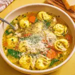 Bowl of chicken tortellini soup with vegetables, spinach, and grated Parmesan cheese