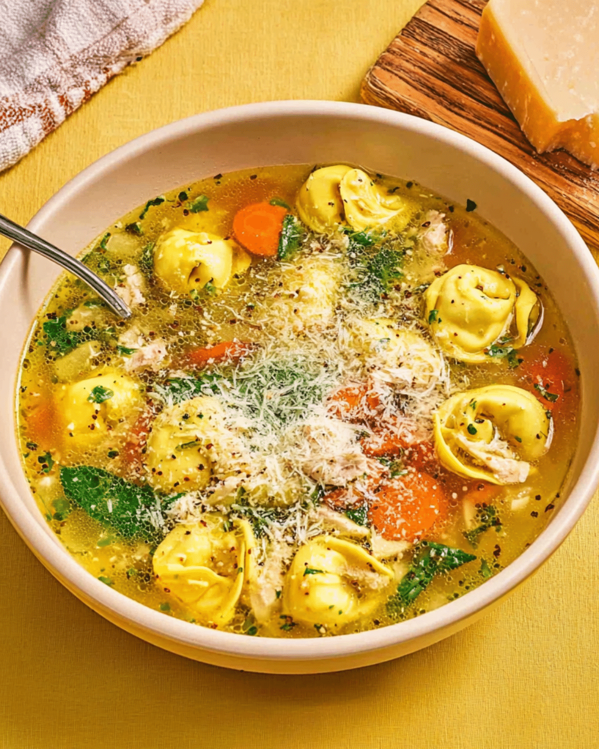 Bowl of chicken tortellini soup with vegetables, spinach, and grated Parmesan cheese