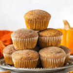 A stack of cinnamon sugar pumpkin muffins arranged on a silver plate, topped with a glistening coating of cinnamon sugar.