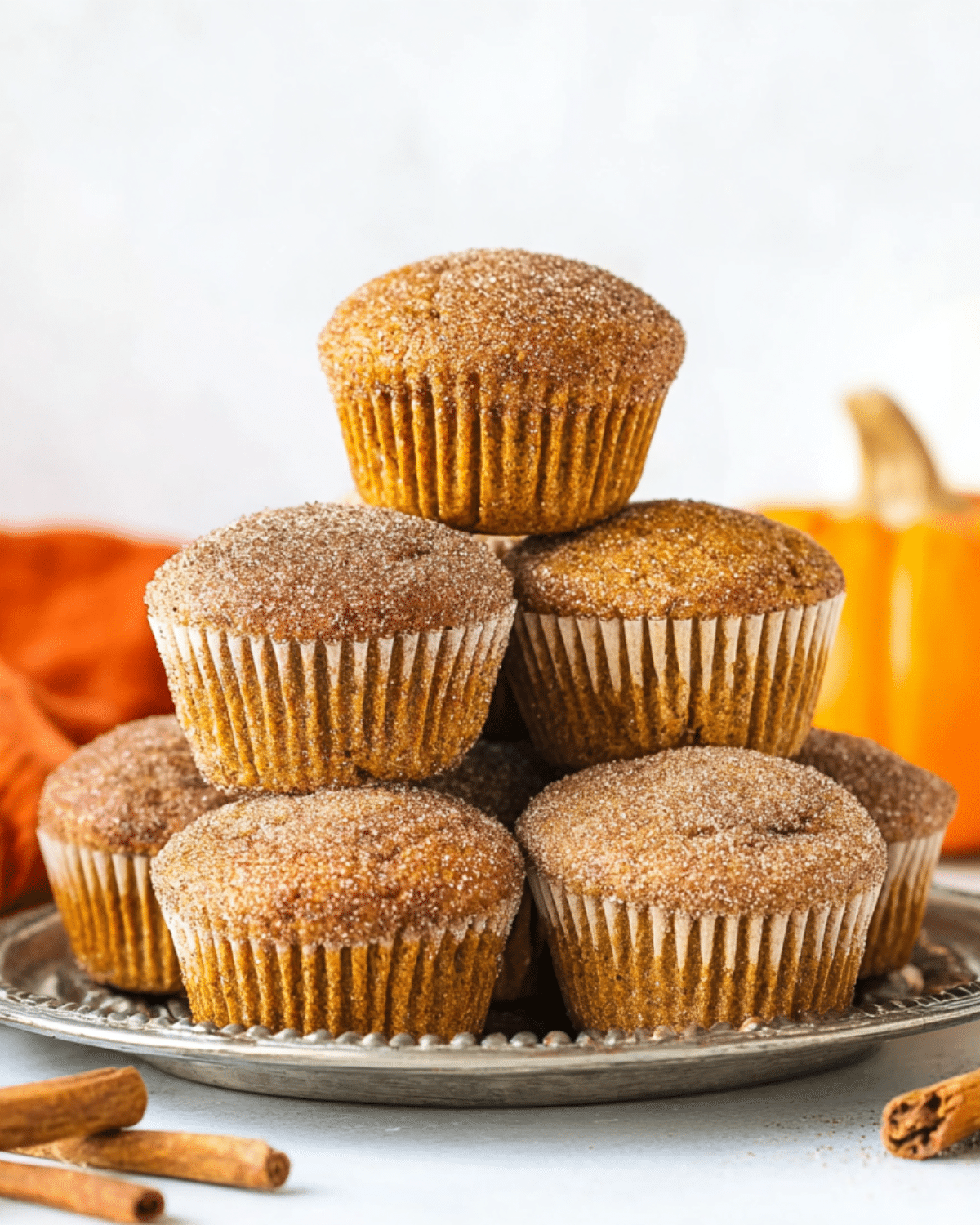A stack of cinnamon sugar pumpkin muffins arranged on a silver plate, topped with a glistening coating of cinnamon sugar.