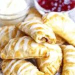 Golden-brown Cookie Empanadas drizzled with icing, filled with fruit jam, and served with whipped cream and jam.
