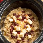 Cranberry Apple Crockpot Oatmeal topped with diced apples and dried cranberries in a black slow cooker.