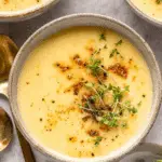 Creamy potato soup in a rustic bowl, garnished with crispy bits, black pepper, and fresh microgreens.