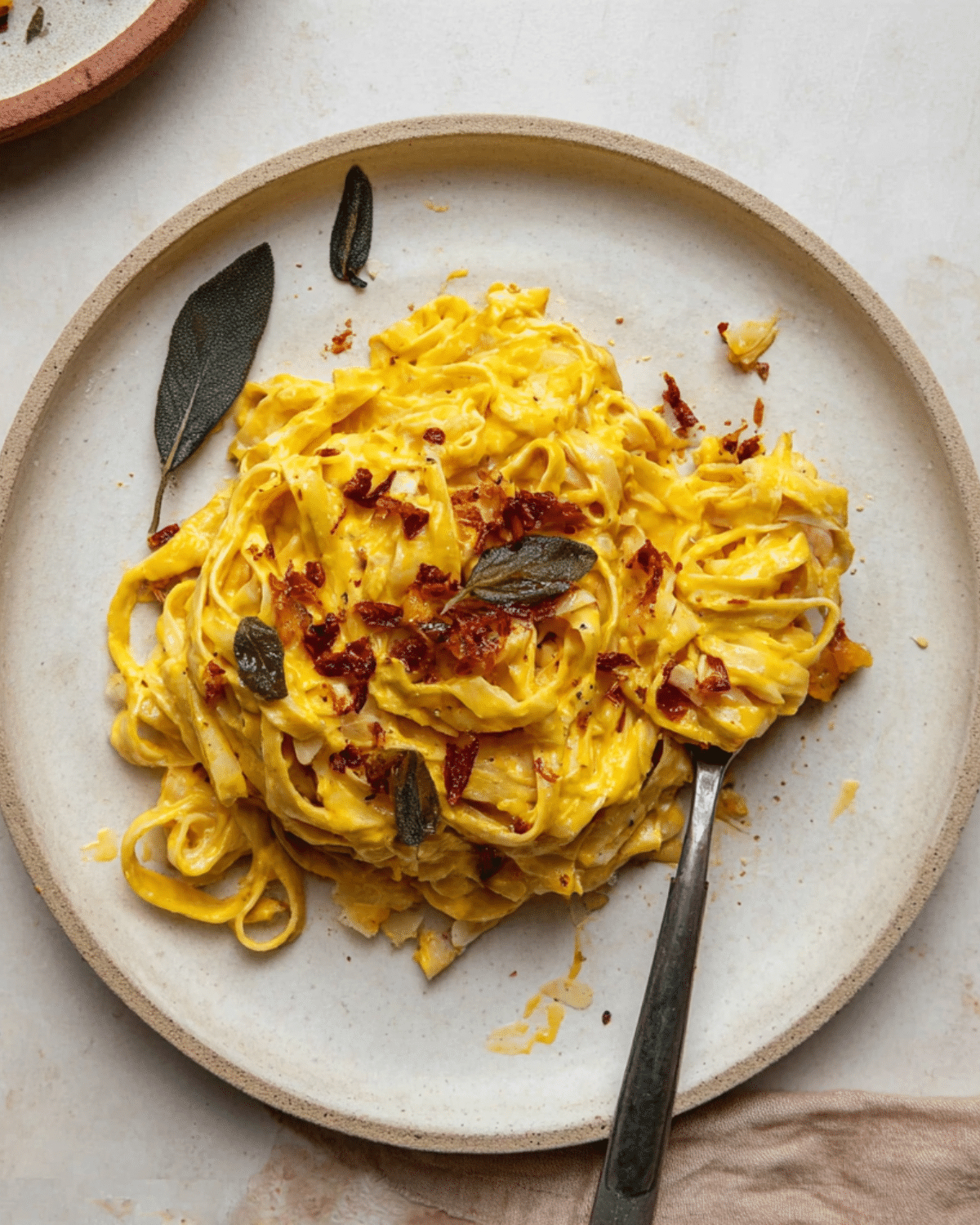 A plate of creamy roasted garlic butternut squash pasta topped with crispy sage leaves and crumbled bacon.