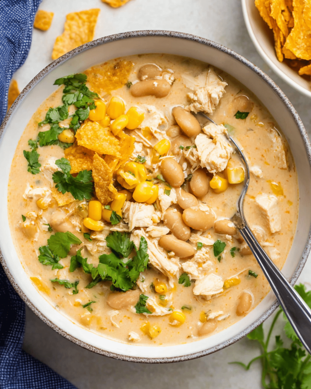 A bowl of creamy white chicken chili filled with shredded chicken, white beans, corn, and garnished with cilantro and crushed tortilla chips.