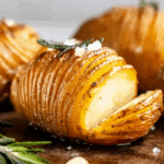 Close-up of crispy Hasselback potatoes garnished with rosemary, garlic, and sea salt.