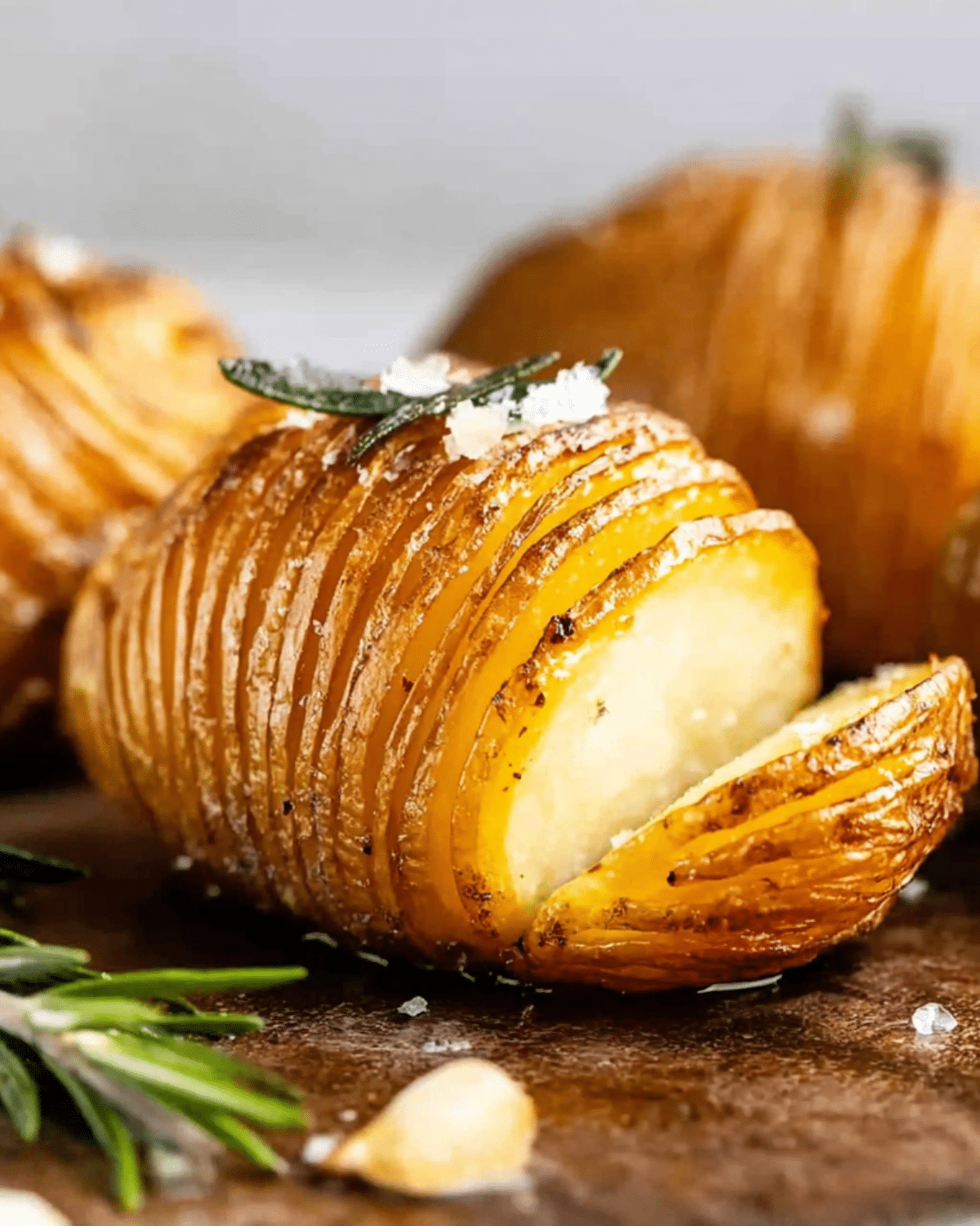 Close-up of crispy Hasselback potatoes garnished with rosemary, garlic, and sea salt.