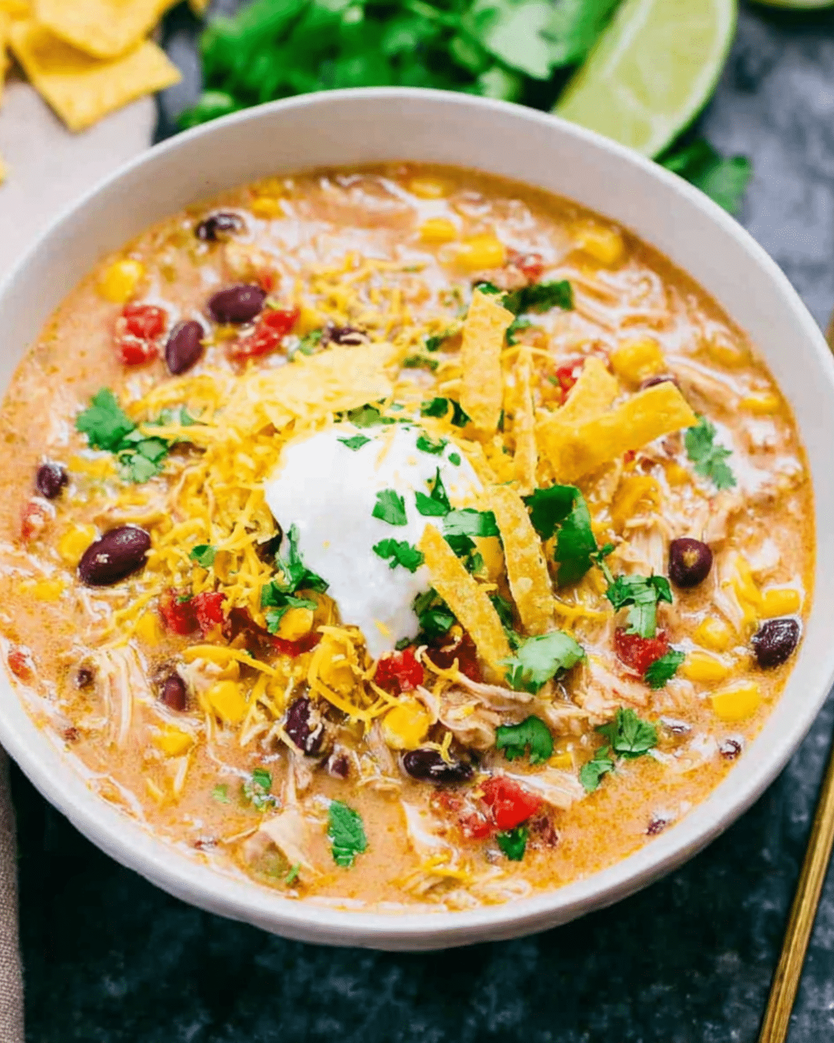 Bowl of Crockpot Chicken Tortilla Soup topped with shredded cheese, sour cream, tortilla strips, and fresh cilantro.