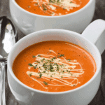 White mug filled with easy creamy tomato soup topped with cream drizzle and herbs