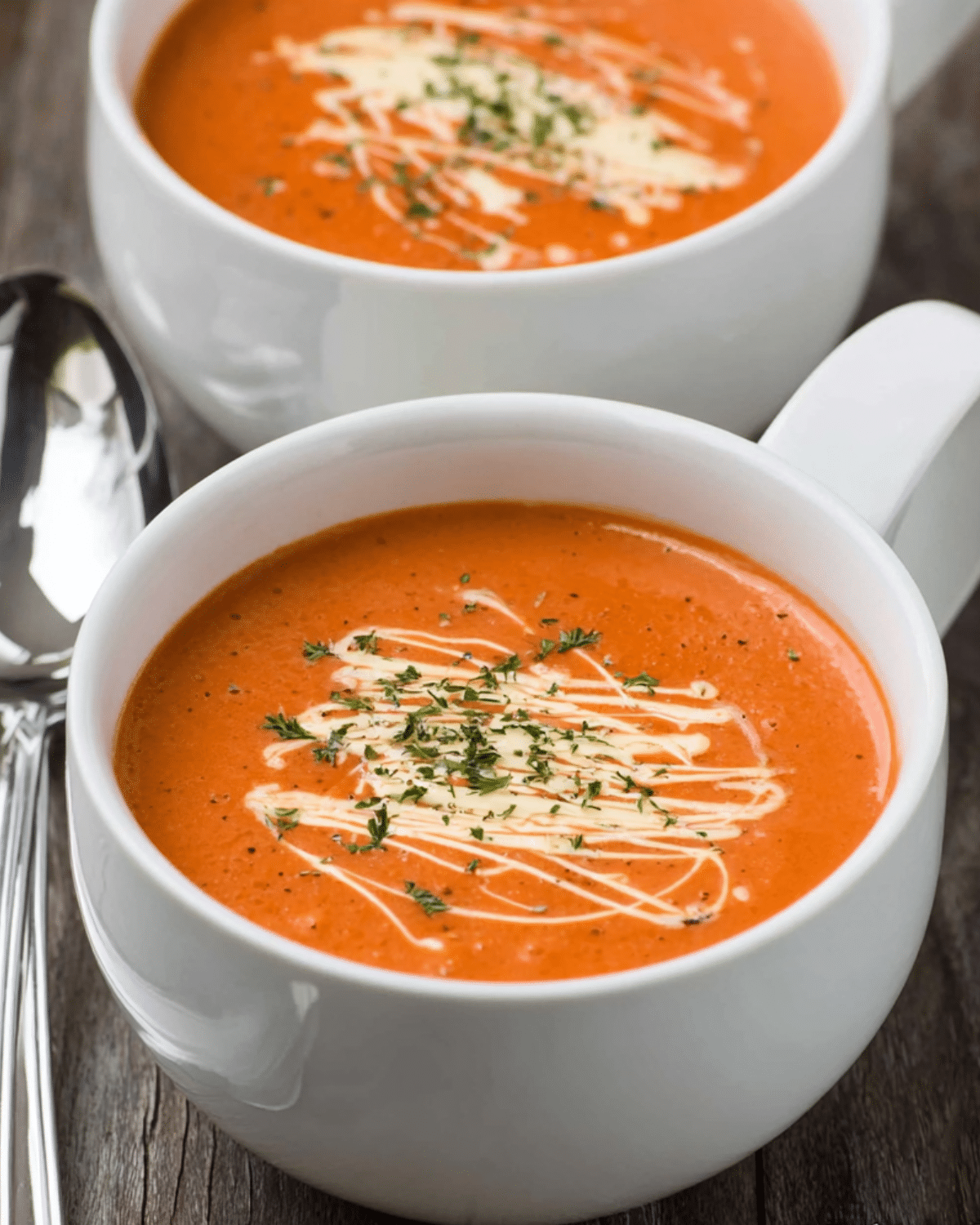 White mug filled with easy creamy tomato soup topped with cream drizzle and herbs