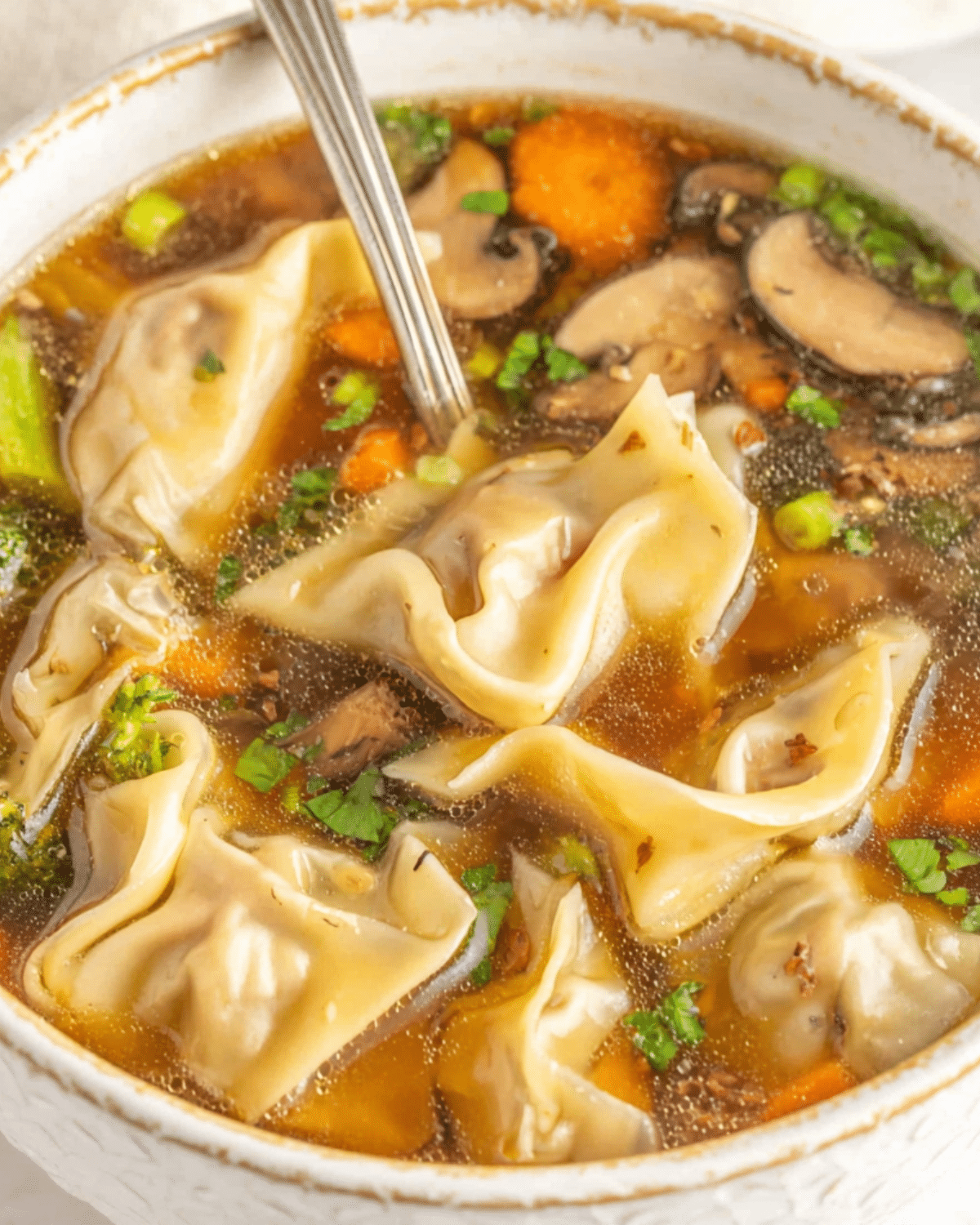 Easy potsticker soup with dumplings, mushrooms, carrots, peas, and herbs in a clear broth, served in a white bowl.