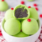 Bright green Grinch Christmas Truffles in a white bowl, topped with red candy hearts and filled with dark chocolate cookie crumbs.