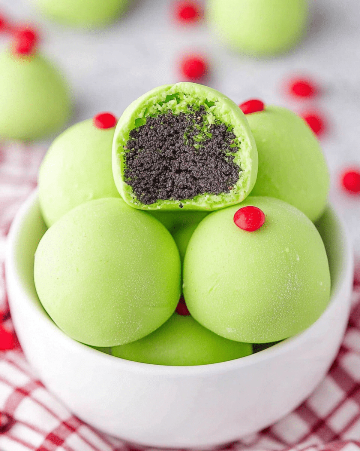 Bright green Grinch Christmas Truffles in a white bowl, topped with red candy hearts and filled with dark chocolate cookie crumbs.