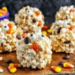 Festive Halloween Popcorn Balls decorated with candy eyes, candy corn, and colorful candies, displayed on a wooden board.