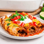 Plate of lazy enchiladas filled with seasoned meat, topped with melted cheese, sour cream, chopped tomatoes, and cilantro.