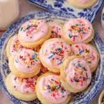Plate of Lofthouse Cookies topped with pink frosting and rainbow sprinkles.