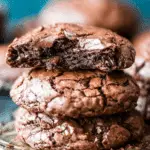 Stack of gooey Magic Brownie Cookies with a fudgy center and crackly tops, one with a bite taken out.