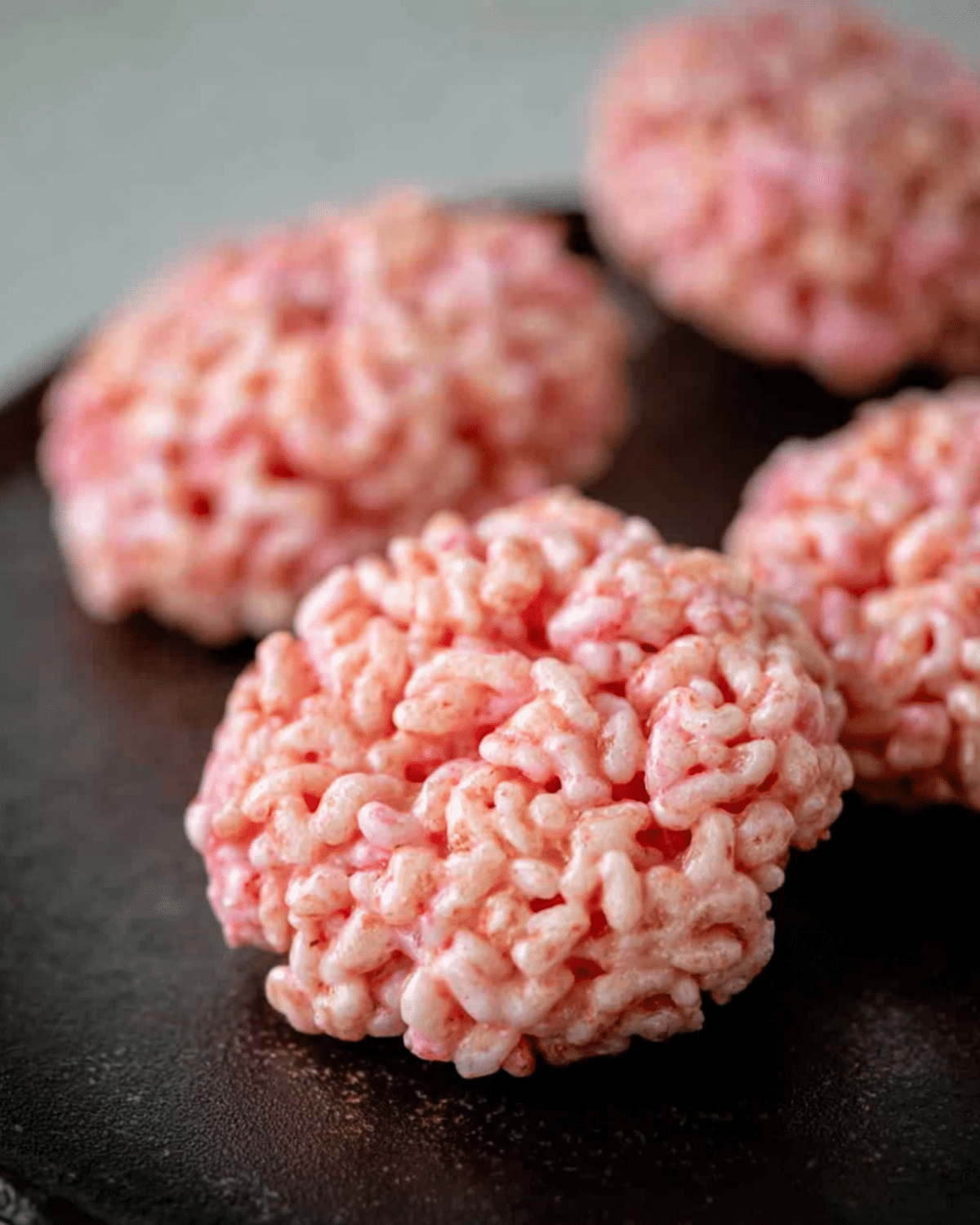 Close-up of Marshmallow Rice Krispies Halloween Brains shaped like pink brains on a dark surface.