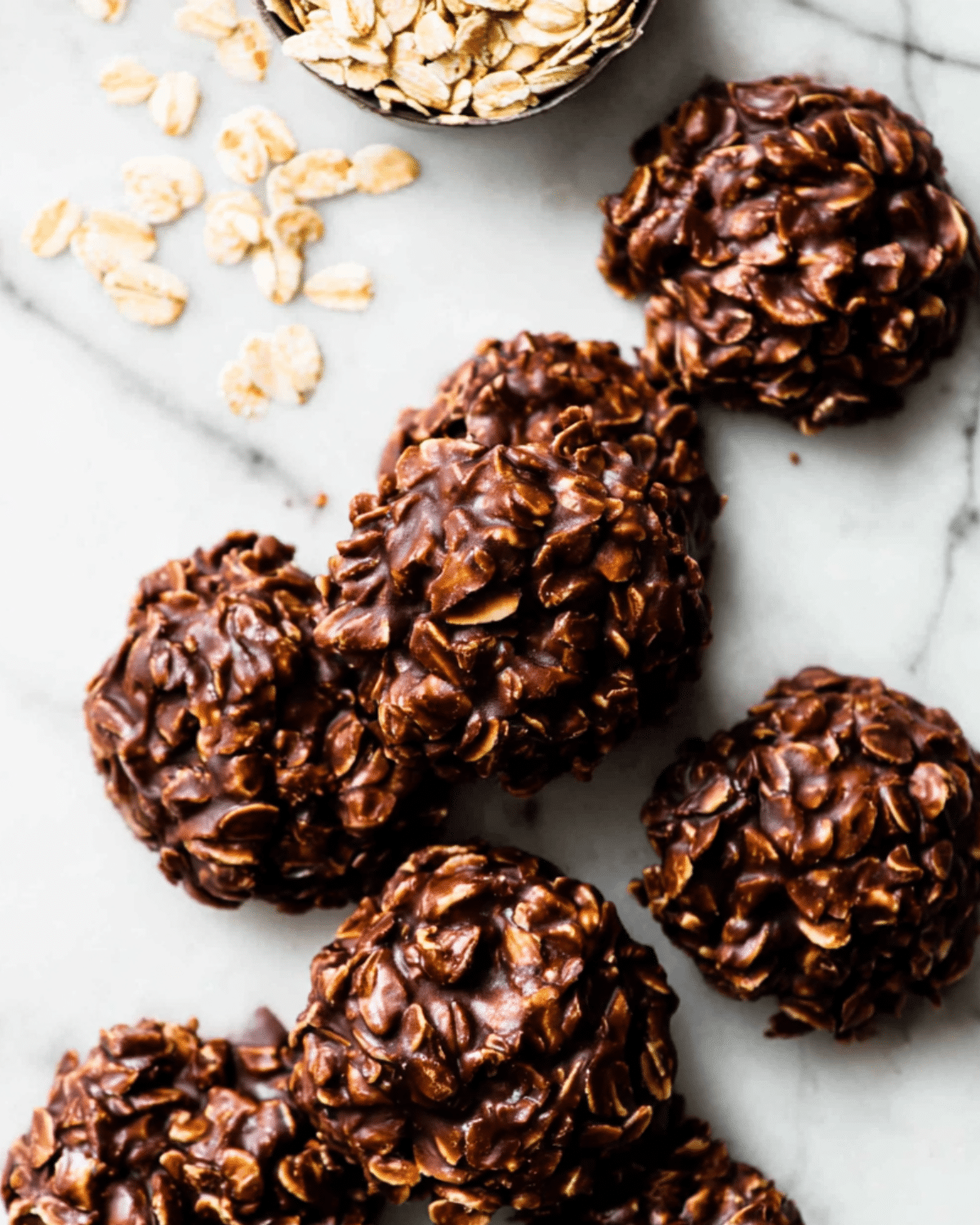 No-bake chocolate peanut butter cookies made with oats, arranged on a marble surface with raw oats scattered nearby.