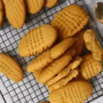 Homemade Nutter Butter Cookies with signature criss-cross pattern, cooling on a wire rack with some broken open to reveal a creamy peanut butter filling.
