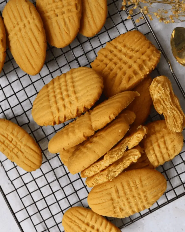 Homemade Nutter Butter Cookies with signature criss-cross pattern, cooling on a wire rack with some broken open to reveal a creamy peanut butter filling.