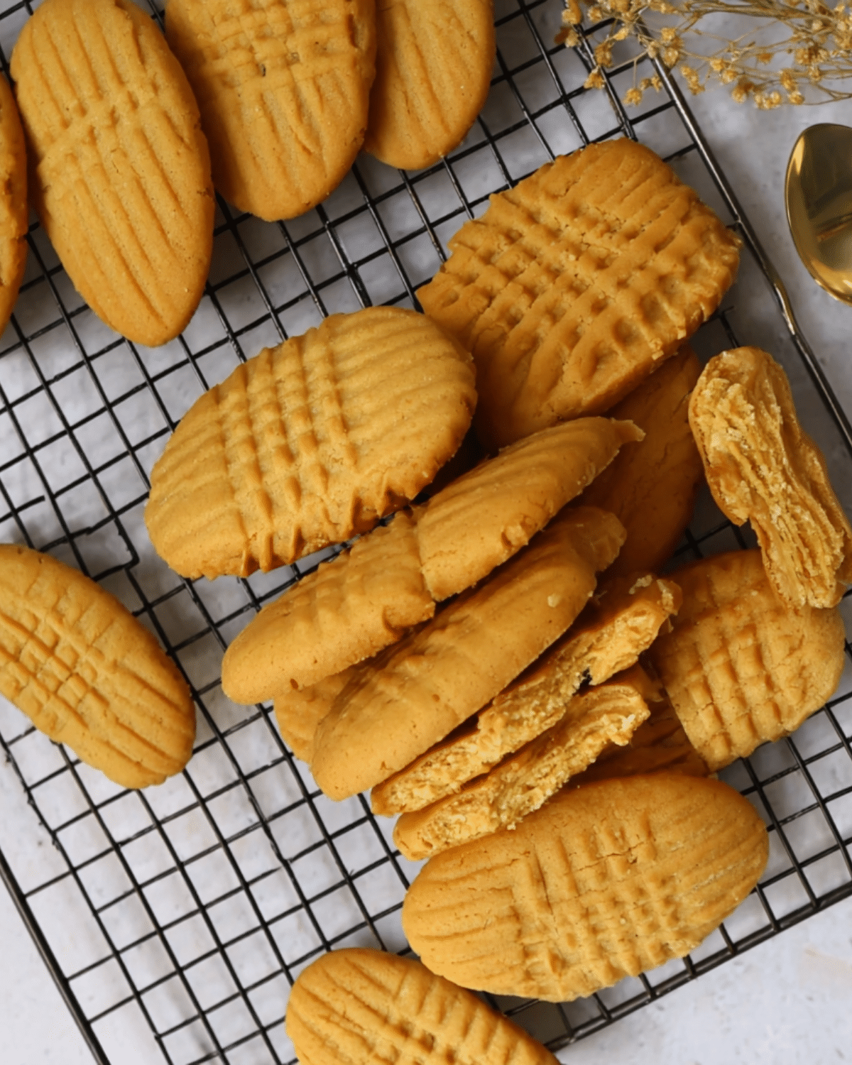 Homemade Nutter Butter Cookies with signature criss-cross pattern, cooling on a wire rack with some broken open to reveal a creamy peanut butter filling.