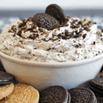Creamy OREO dip in a white bowl topped with crushed OREO cookies, surrounded by chocolate and golden OREO cookies.