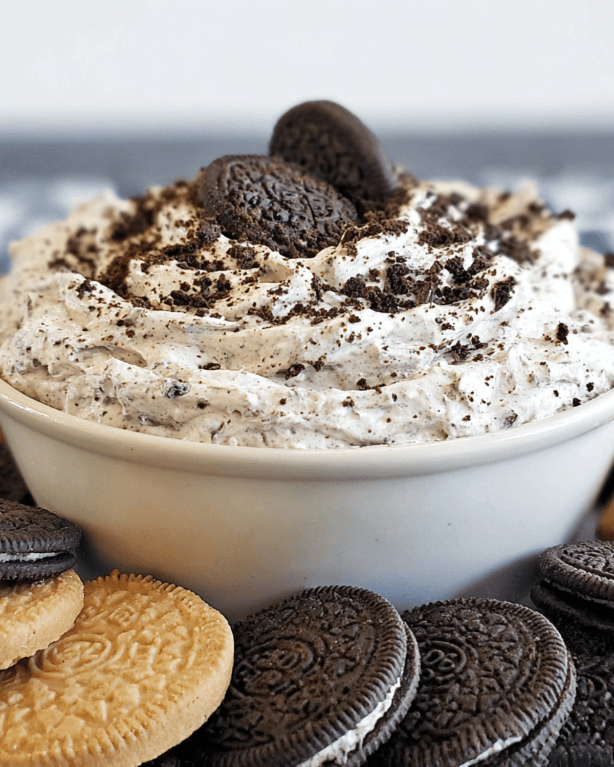 Creamy OREO dip in a white bowl topped with crushed OREO cookies, surrounded by chocolate and golden OREO cookies.
