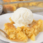 A serving of pineapple dump cake topped with a scoop of vanilla ice cream on a white plate with a golden fork.