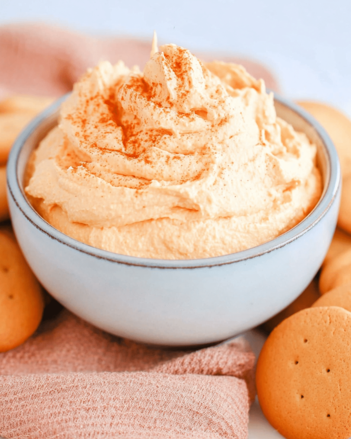 Creamy Pumpkin Pie Dip in a light blue bowl, topped with a sprinkle of cinnamon and surrounded by vanilla wafers.