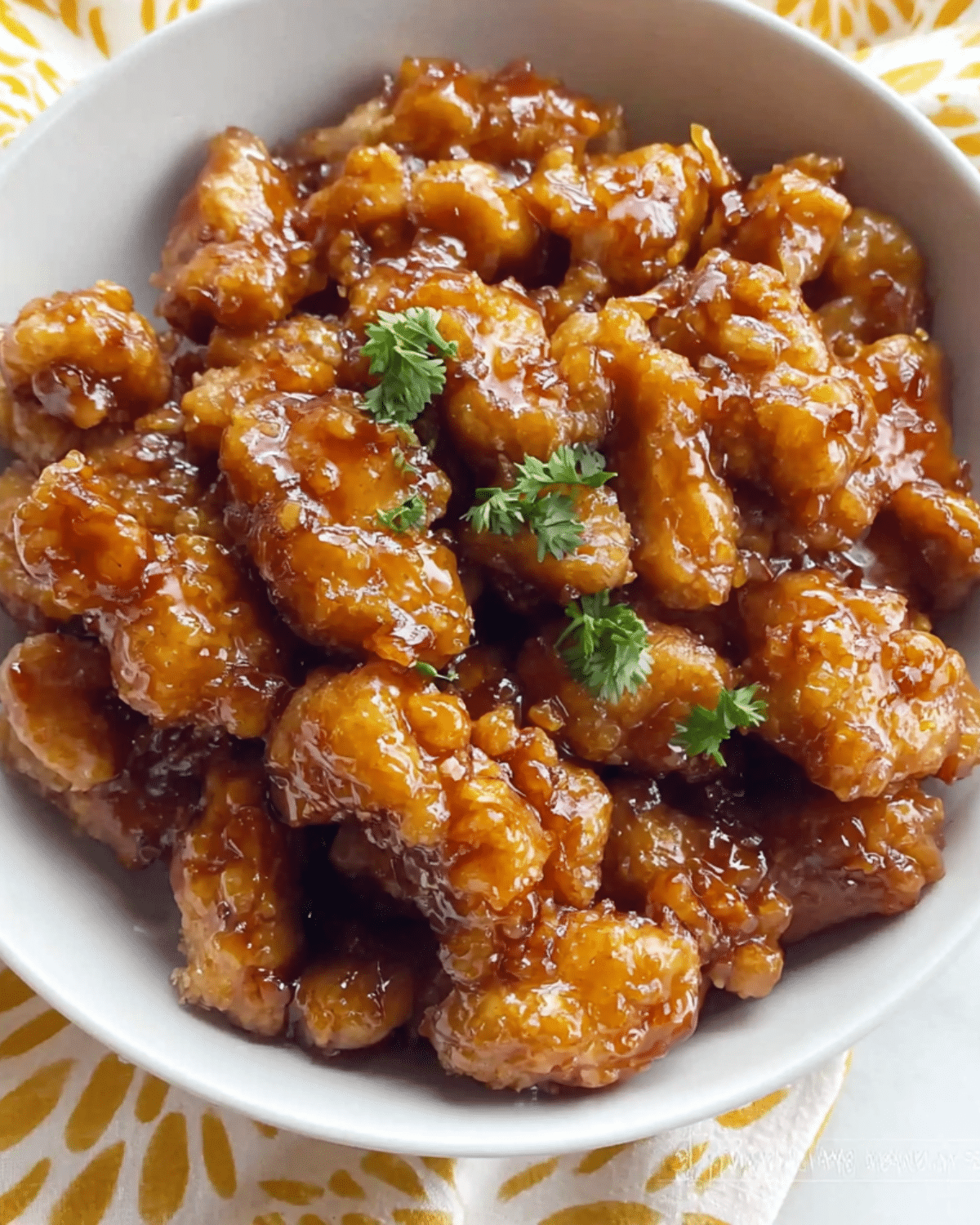 Bowl of crispy Panda Express Orange Chicken coated in a glossy orange sauce and garnished with fresh parsley.