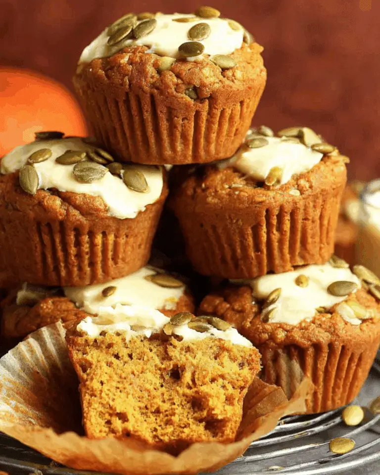 Pumpkin cream cheese muffins topped with pumpkin seeds, with one muffin cut open to reveal a moist interior.