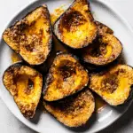 Plate of golden roasted acorn squash halves caramelized with brown sugar and butter, served on a white dish.