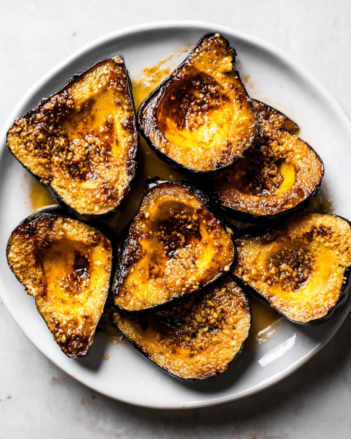 Plate of golden roasted acorn squash halves caramelized with brown sugar and butter, served on a white dish.