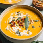 Bowl of roasted butternut squash soup garnished with cream, sage, pumpkin seeds, and sun-dried tomatoes.