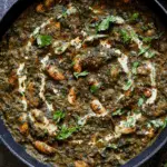 A skillet filled with saag butter beans, garnished with fresh cilantro, cream swirls, and red chili flakes.