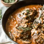 Close-up of Salisbury Steak recipe served in a cast iron skillet with mushroom gravy and fresh thyme.