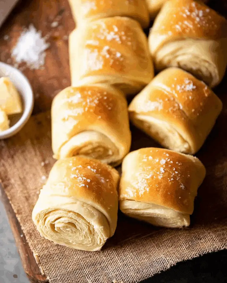 Golden Salted Honey Butter Parker House Rolls topped with flaky sea salt, arranged on a wooden board.
