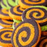 Bright orange and black spiral Halloween cookies stacked together, with a few green-accented cookies in the background.