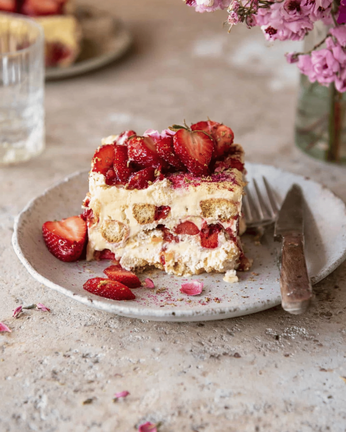 A slice of strawberry tiramisu layered with mascarpone cream, ladyfingers, and fresh strawberries, served on a ceramic plate with a fork.