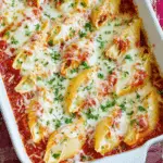 Baking dish filled with cheesy stuffed shells topped with marinara sauce and melted mozzarella, garnished with fresh parsley.
