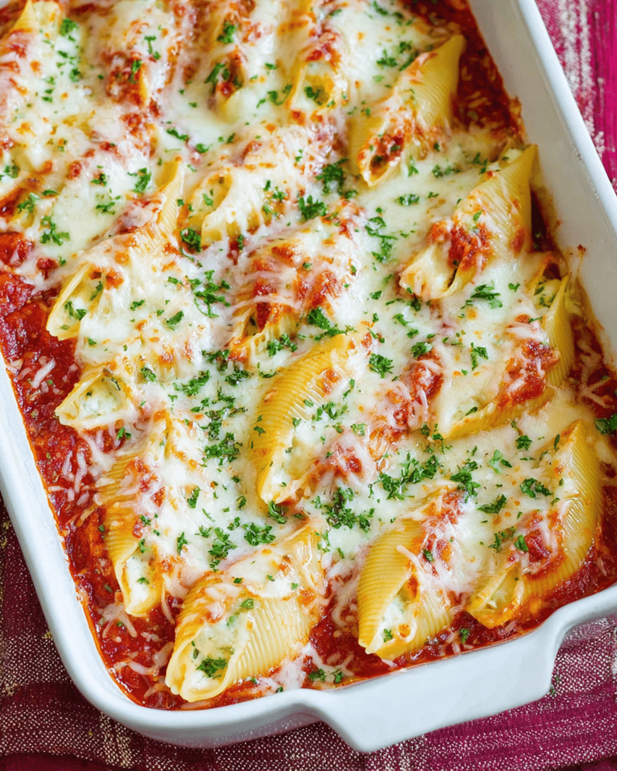 Baking dish filled with cheesy stuffed shells topped with marinara sauce and melted mozzarella, garnished with fresh parsley.