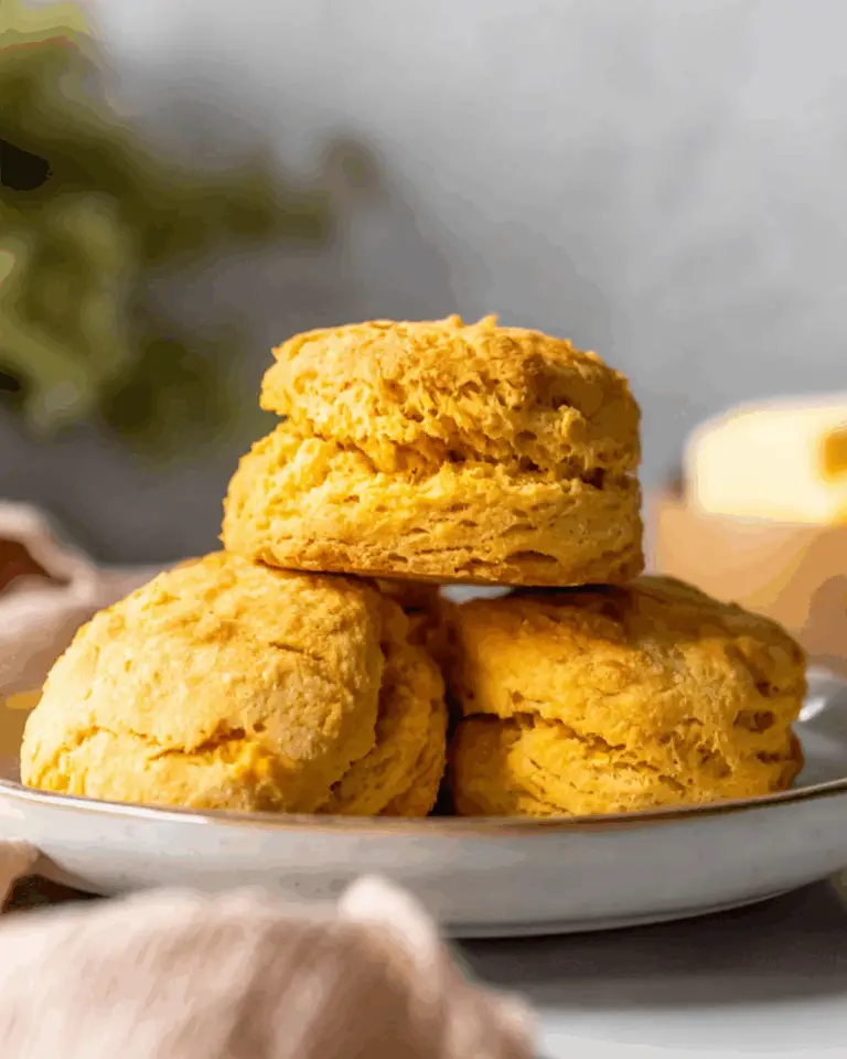 Fluffy sweet potato biscuits stacked on a white plate, with a soft golden-brown crust.
