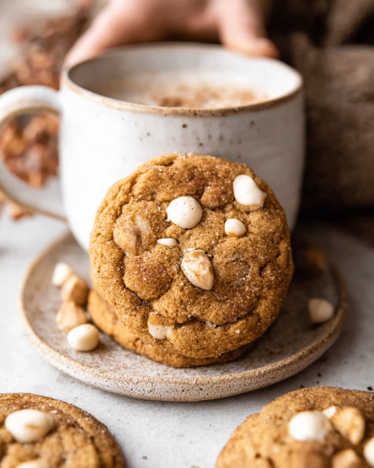 White chocolate chai pumpkin snickerdoodle cookie leaning against a ceramic mug filled with a frothy drink.