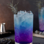Chilled glass of Witches Brew Lemonade with layered purple and blue hues, garnished with a sprig of rosemary and served over ice.