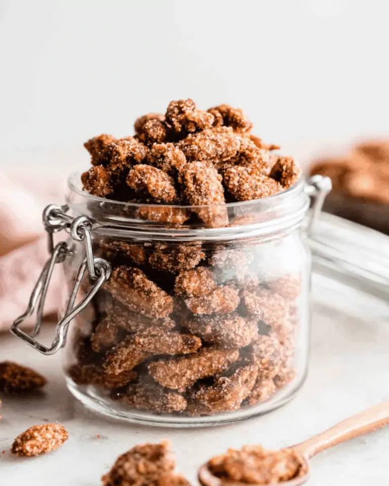 Glass jar filled with crunchy candied almonds coated in a cinnamon-sugar mixture, with a few almonds scattered around.