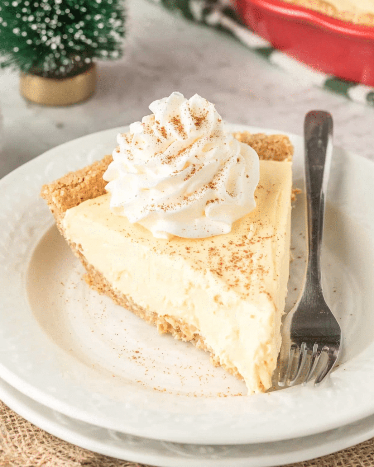 Slice of creamy eggnog pie with whipped cream and a sprinkle of nutmeg on a white plate.