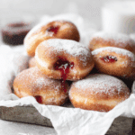 Tray of homemade jelly donuts dusted with powdered sugar, filled with raspberry jelly.
