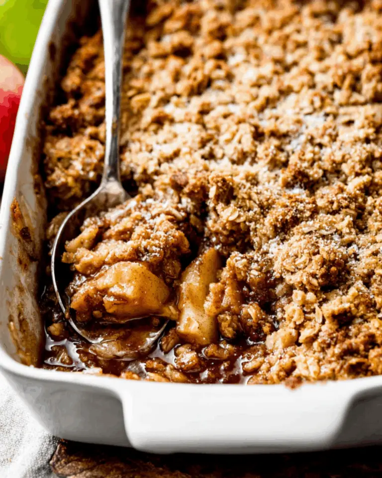 Homemade apple crisp with a golden oat topping, served warm in a white baking dish with a spoon.
