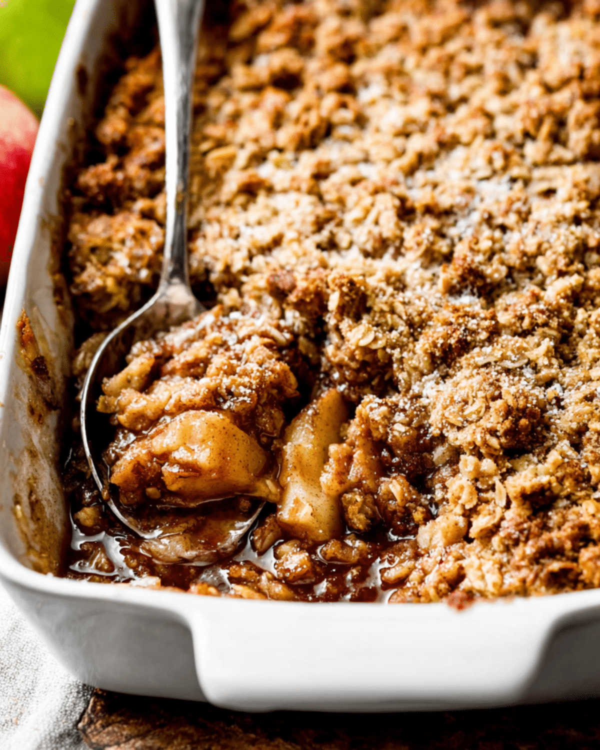 Homemade apple crisp with a golden oat topping, served warm in a white baking dish with a spoon.